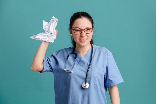 파란색 배경 위에 서 있는 분노에 종이를 구겨 목 주위에 청진기와 의료 유니폼에 젊은 여자 간호사