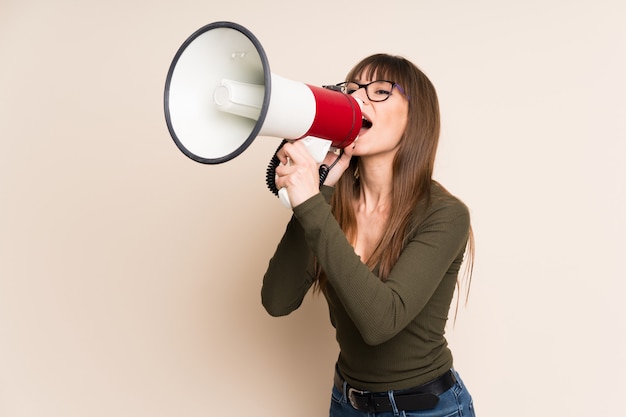 Young woman on ocher shouting through a megaphone