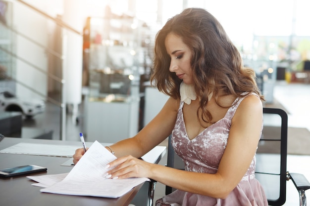 Young woman at the office signs documents.