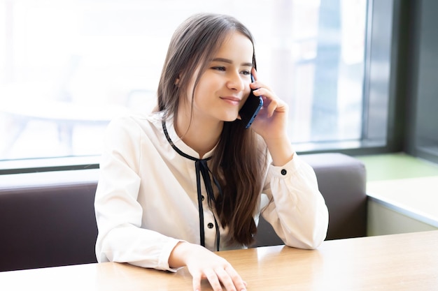 Young woman office worker in a cafe with a smartphone, talking, smiling