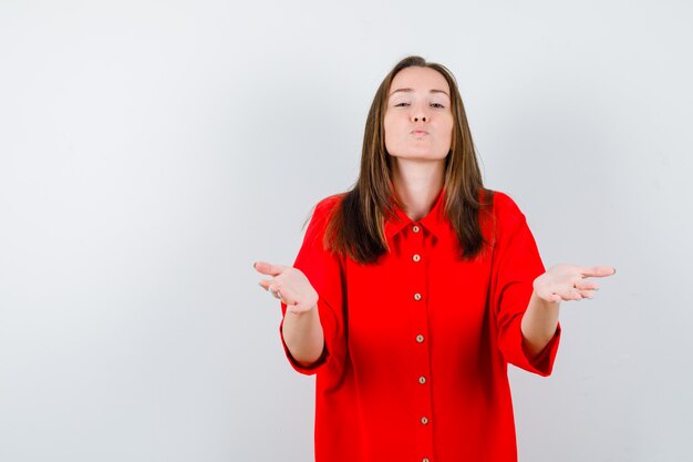 Young woman opening arms for hug, pouting lips in red blouse and looking peaceful , front view.