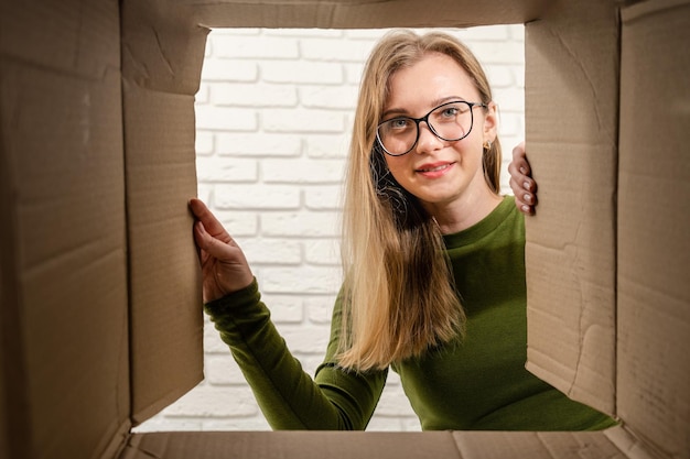 Foto giovane donna che apre una scatola di cartone e guarda all'interno consegna del pacco disimballato