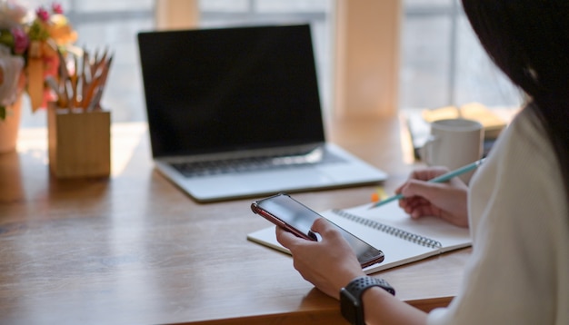 Young woman operating a smartphone and taking notes