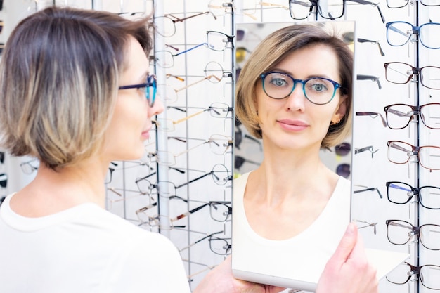 Young woman in optic store choosing new glasses with optician. glasses in the store of optics. A woman chooses glasses. Emotions. Ophthalmology.