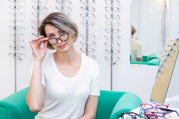 眼鏡店で眼鏡店で新しい眼鏡を選ぶ若い女性。光学の店の眼鏡。女性は眼鏡を選びます。感情。眼科。