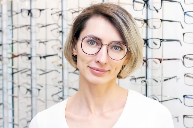 Young woman in optic store choosing new glasses with optician