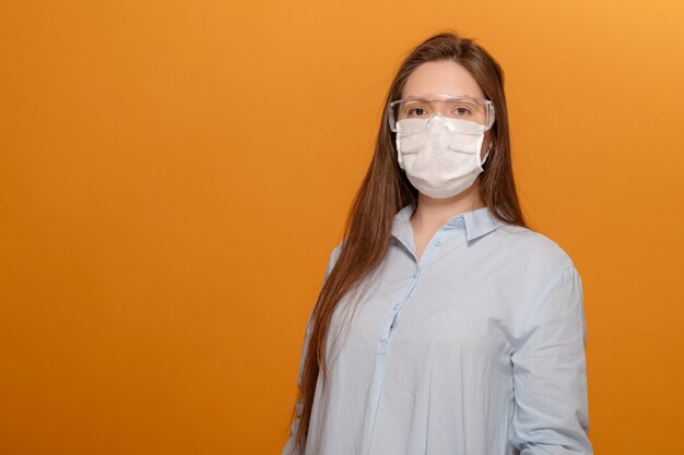 Young woman on orange wall in protective medical mask