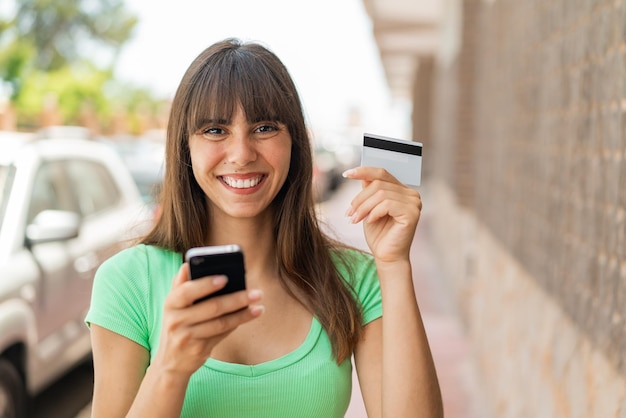 Young woman at outdoors buying with the mobile with a credit card