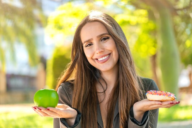 Photo young woman at outdoors holding apple and donut with happy expression