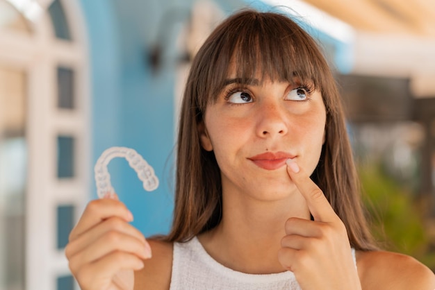 Photo young woman at outdoors holding invisible braces and thinking