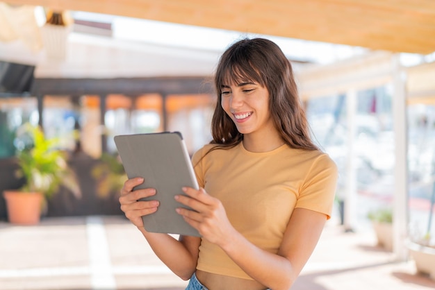 Young woman at outdoors holding a tablet with happy expression