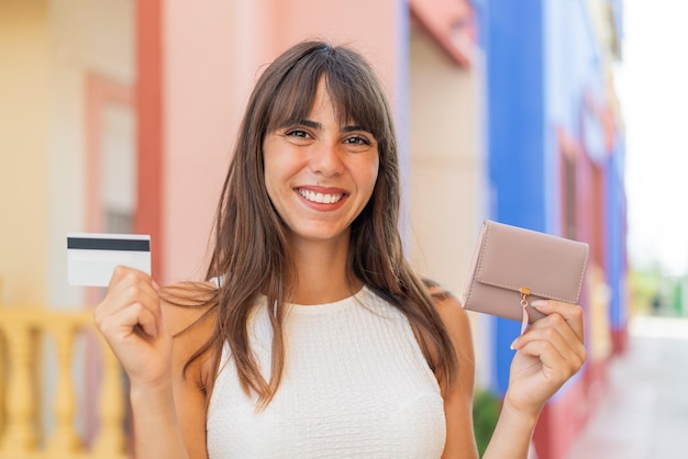 Молодая женщина на улице с кошельком и кредитной картой со счастливым выражением лица