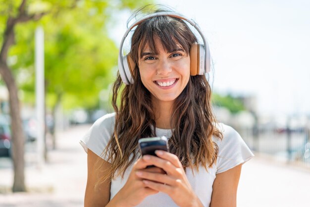 Young woman at outdoors listening music with a mobile and looking front