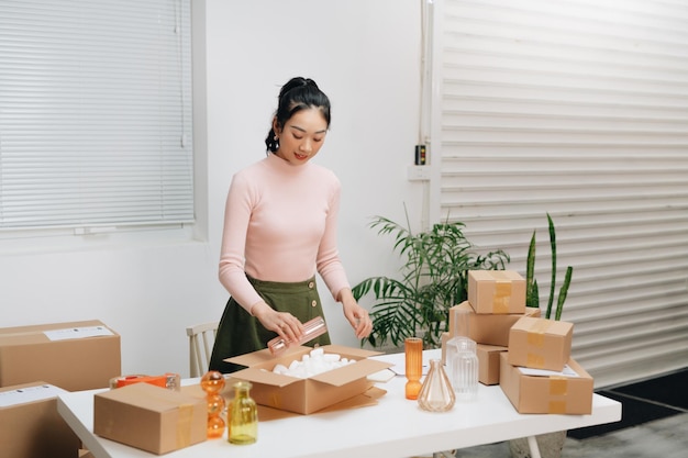 Young woman owener of small business packing product in boxes preparing it for delivery