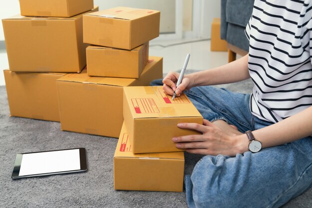 young woman owner working and packing on box to customer at the sofa in home office, seller prepares the delivery.