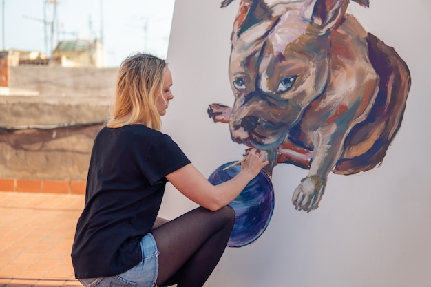 Artista della pittura della giovane donna che disegna a casa il tetto. immagine di bulldog su grande tela. arte all'aperto