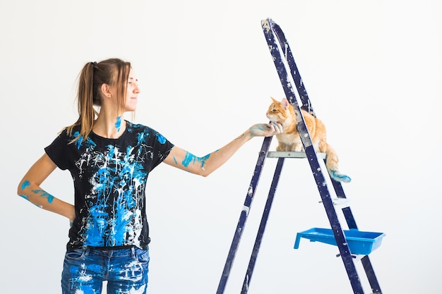 Young woman painter stroking a cat, designer and worker paints the wall.