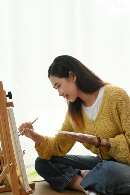 Young woman painting on a canvas at home