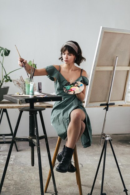 Photo young woman painting on canvas while sitting on table