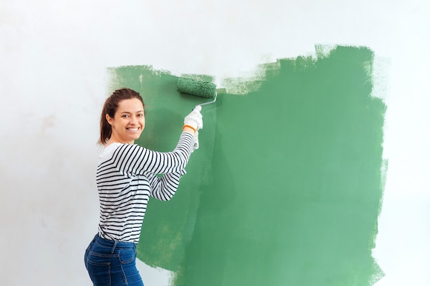 Young woman painting interior wall with paint roller