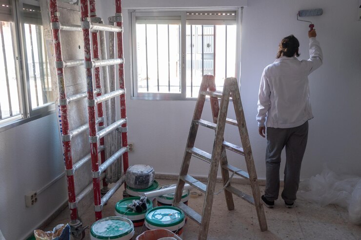 Young woman painting interior wall with white paint paint cans and painter ladder