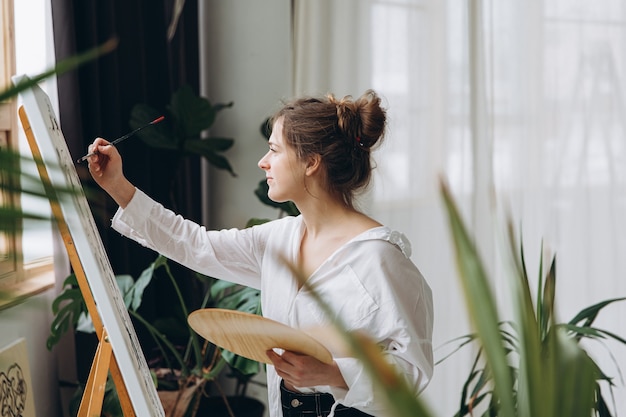 Молодая женщина рисует кистью на мольберте