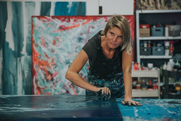 写真 若い女性は、彼女のインテリアスタジオの作業台に彼女の手とヘラで抽象絵画を描きます。