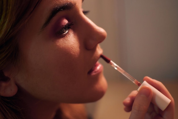 Young woman paints her lips in front of her bedroom mirror