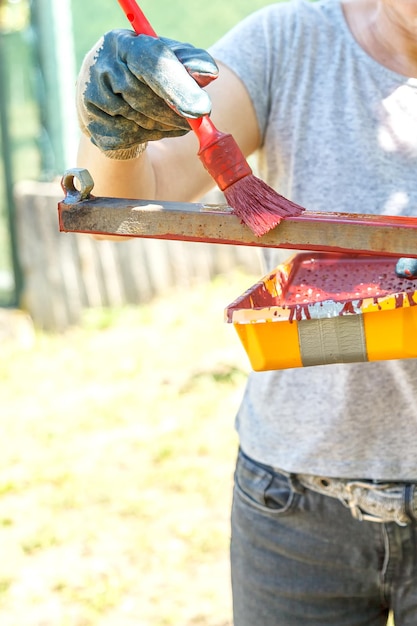 Young woman paints red primer metal structure