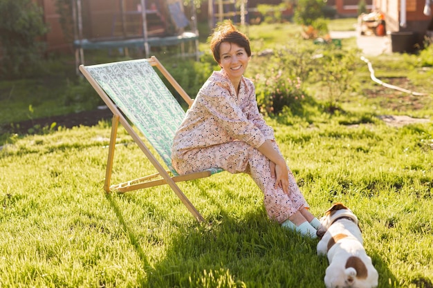 Young woman in pajama is resting in chair on a green lawn on sunny summer day village and country life