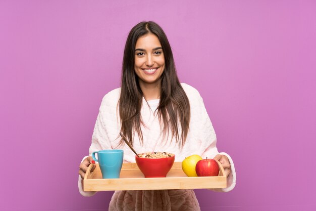 Young woman in pajamas and dressing gown over isolated purple wall