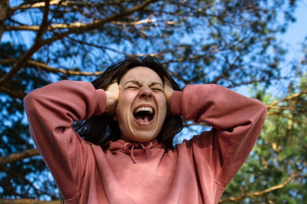 A young woman in a panic, grabbed her head with her hands and screams loudly, closes her eyes.