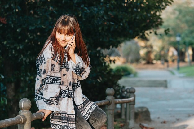 Young woman in the park during a phone call smiling receiving\
good news on trendy and modern clothes with copy space to add your\
advertisement or copy text.blurred background confidence towards\
future