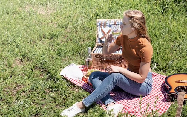 Giovane donna nel parco fuori in una giornata di sole godendosi l'estate sognando e bevendo vino