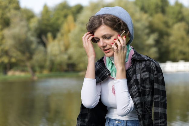 Young woman in the park speaks by mobile phone. Cute girl portrait in french style.