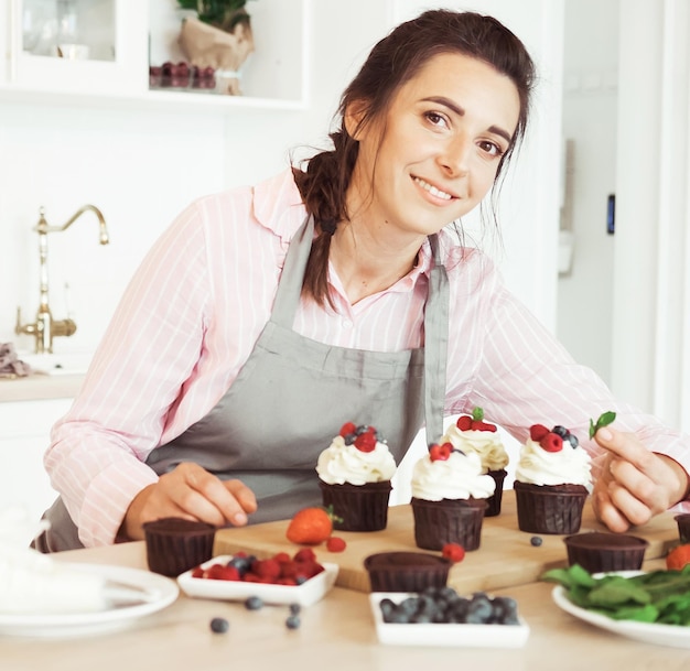 若い女性パティシエがカップケーキを飾る