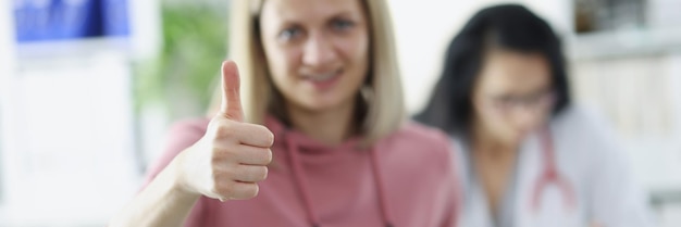 Young woman patient holds thumbs up at doctor appointment quality healthcare concept