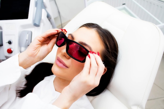 A young woman patient is lying in glasses at the beautician's office.