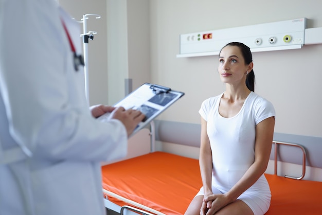 Young woman patient sitting on couch in hospital in front of doctor with clipboard treatment of