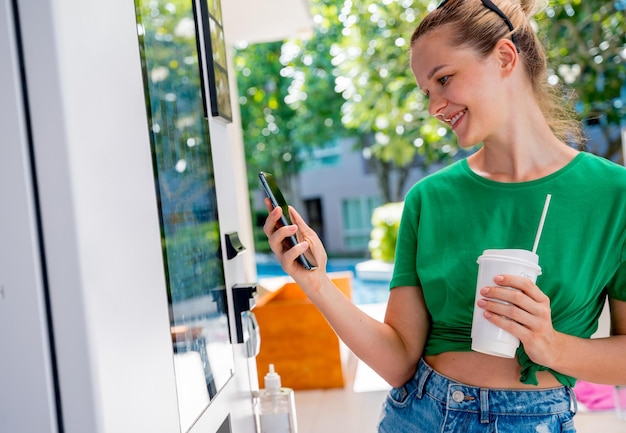 Young woman paying for coffee at vending machine using contactless method of payment