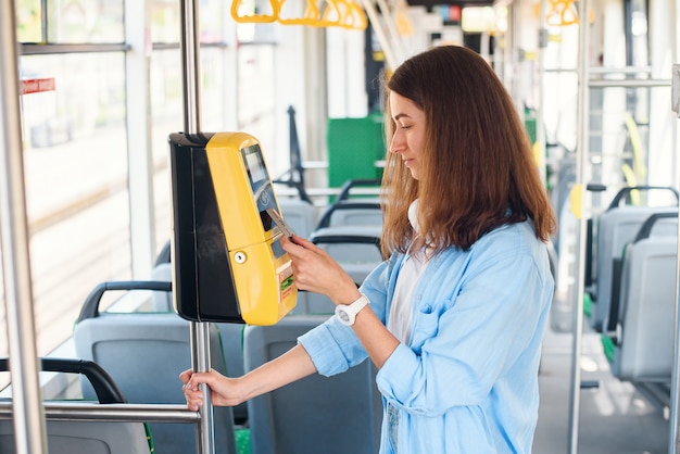 Young woman pays by bank card for the public transport in the tram or subway.