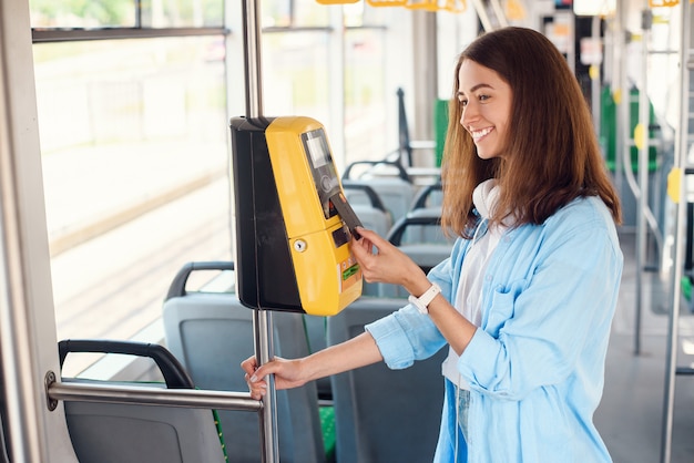 Молодая женщина оплачивает банковской картой общественный транспорт в трамвае или метро.