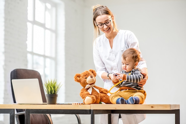 Young woman pediatrician taking care of a baby boy sitting on the table at the office