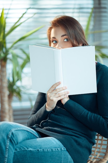 Young woman peeks from behind a book with a blank cover