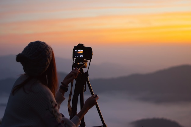 Young woman photographer taking picture of landscape when sunrise  at mountain peak.