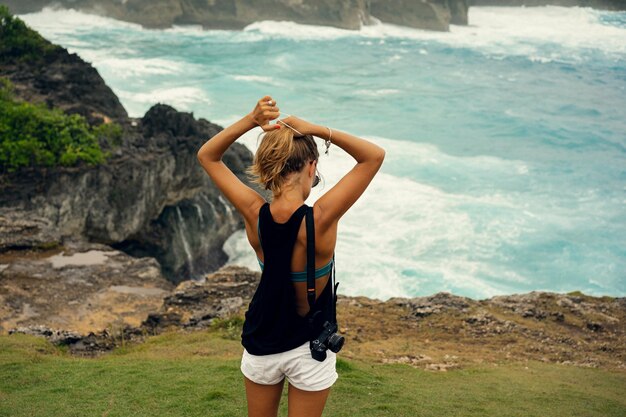 Young woman photographer traveler with a camera on the edge of a cliff takes pictures of nature