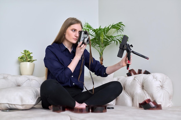 Young woman photographer with vintage camera recording video on smartphone