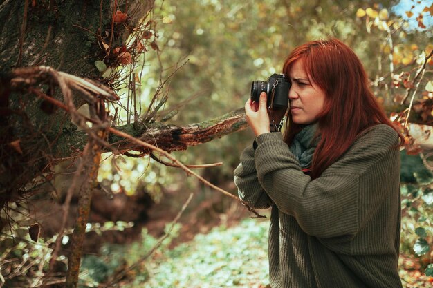 Foto giovane donna che scatta foto con la fotocamera mentre è in piedi nella foresta