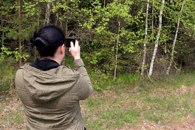 한 젊은 여성이 이른 봄에 공원에서 아름다운 자연을 스마트폰으로 촬영하고 있습니다. 자연과 사진에 대한 관광 카이킹 열정의 개념