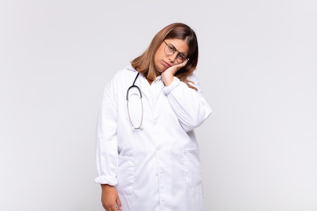 Young woman physician feeling bored, frustrated and sleepy after a tiresome, dull and tedious task, holding face with hand